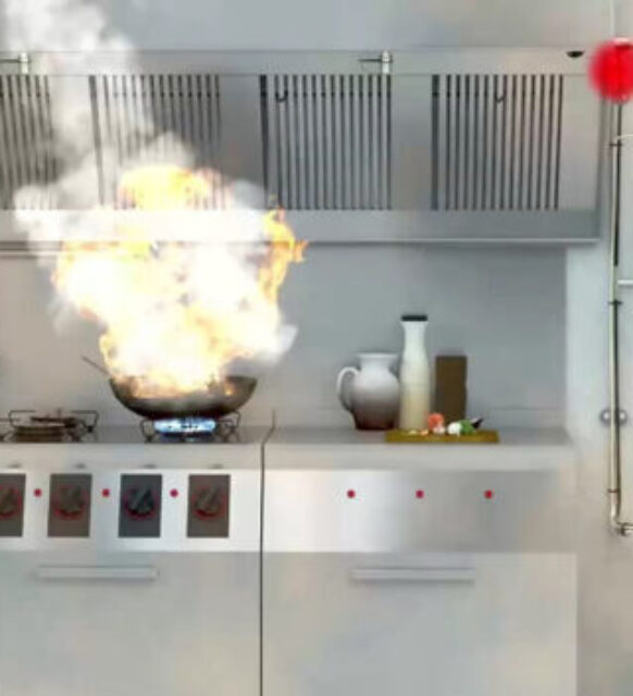 Endüstriyel mutfakta yoğun duman ve alevler yükselirken bir aşçı güvenli bir mesafede duruyor.